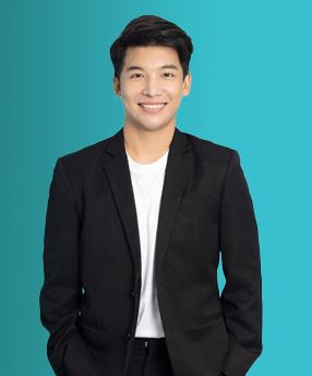 Smiling person in a black suit and white shirt stands against a teal background.